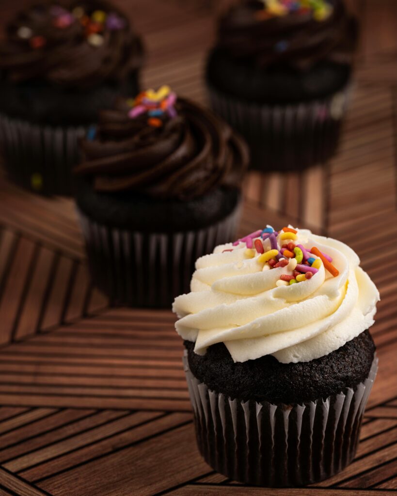 Close-up of chocolate cupcakes topped with creamy icing and vibrant sprinkles on a wooden table.